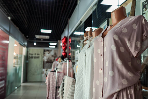 Two well-dressed Thai women in dress are leaving a fashion store in street Pracha Songkhro Rd in Huaei Khwang at night. In windows are dummies with fashion. One woman is carrying  a shopping bag.  In street is  popular night market and has many shops for local fashion and cosmetic shopping.