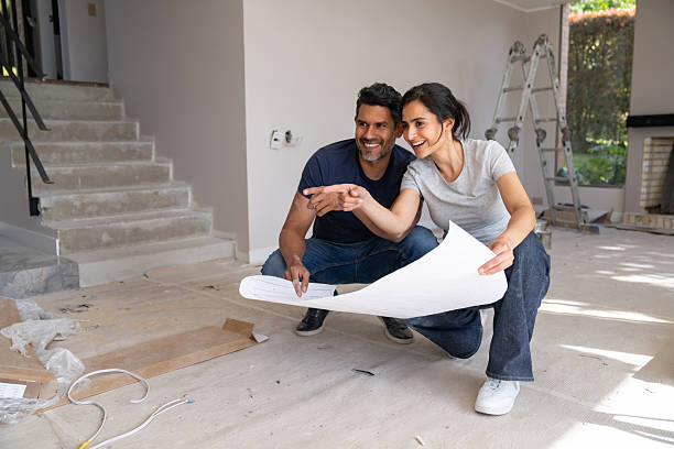 Loving Latin American couple remodeling their house and pointing away while looking at a blueprint