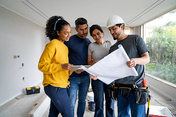 istock Construction worker showing blueprints to a designer and a couple while remodeling a house 2238592445