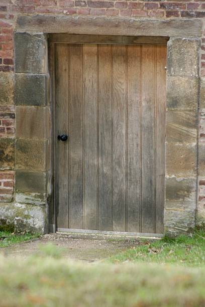 istock A rustic wooden arched door is set into a red brick wall with a stone surround. The setting is peaceful, with soft sunlight filtering through trees, creating a quiet, secluded atmosphere. 2238611714