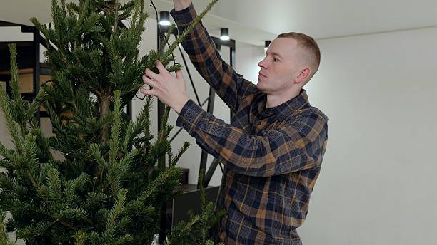 istock Young man decorating christmas tree, stringing festive lights and creating cozy holiday ambiance in contemporary urban living space 2238617371