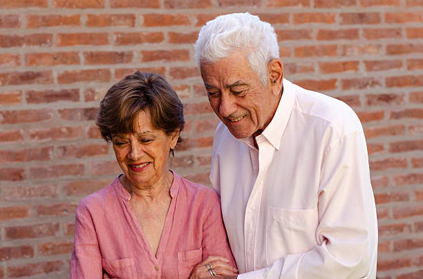 A happy senior couple smiling outdoors on a red bricked wall.