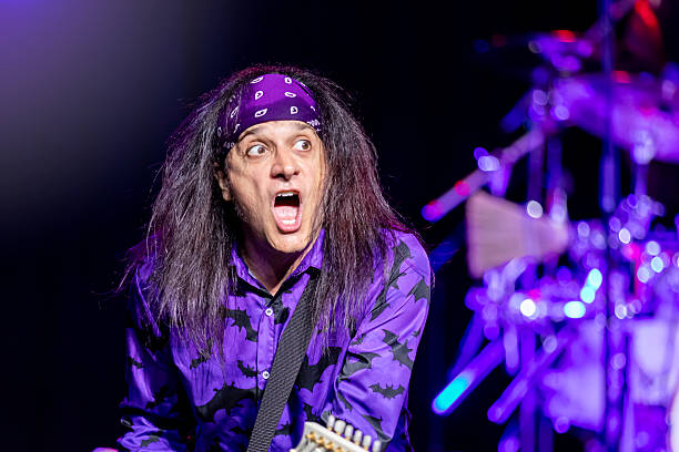 A male rock guitarist singing along as he performs a live concert.