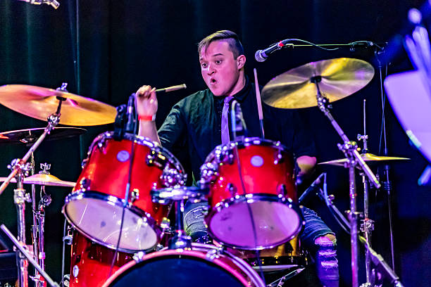 A 26 year old young man intensely plays drums during a concert performance with his pop punk band.