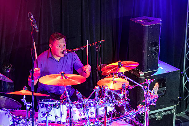 A high angle view of a drummer of a rock band singing into a microphone and playing drums live during a concert performance.