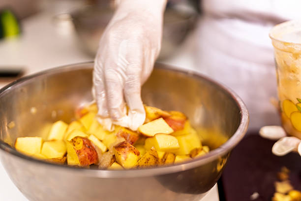 Person wearing gloves preparing fresh chopped fruit in a metal bowl in a restaurant kitchen environment