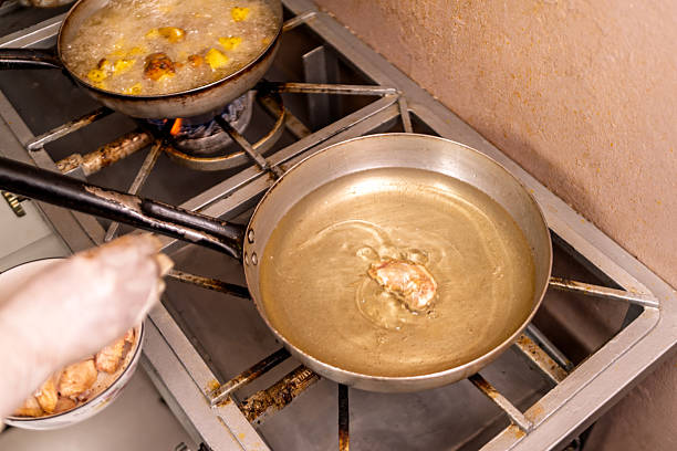 Chef's hands putting food pieces into a sizzling pan of hot oil on a gas stove in a professional kitchen