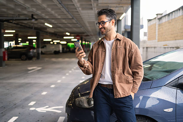 istock Smiling man using smartphone leaning on car in urban parking garage, checking app or messaging 2238634976