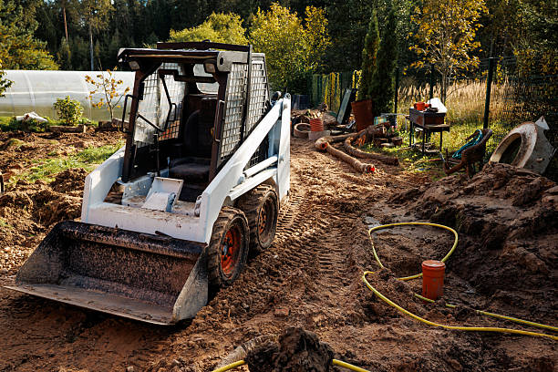 A small crawler track backhoe is moving past palm and cypress trees on a construction site in Southwest Florida.