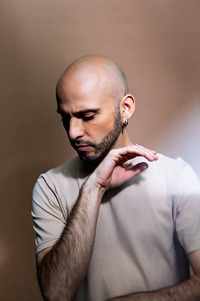 Calm mid adult man posing against brown background. Bald man with facial hair looking down and thinking against studio background.