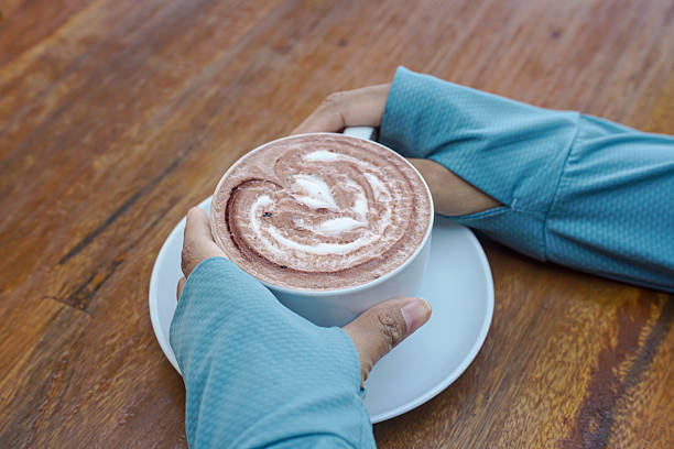 A person is holding a white coffee cup with a heart-shaped design on it