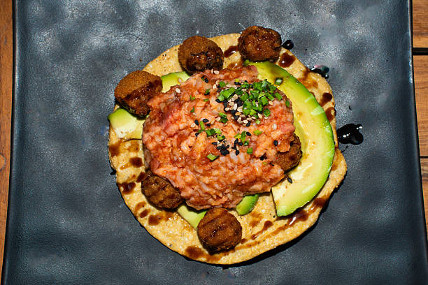 Close-up of a gourmet tuna tostada topped with avocado and spices, served with croquettes. A delicious and colorful dish that combines fresh seafood with authentic Mexican flavors.