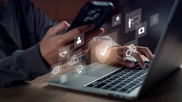 istock Close-up of hands using laptop and smartphone with digital interface icons symbolizing workplace security, digital governance, compliance monitoring, and risk control in a modern tech environment. 2238654911