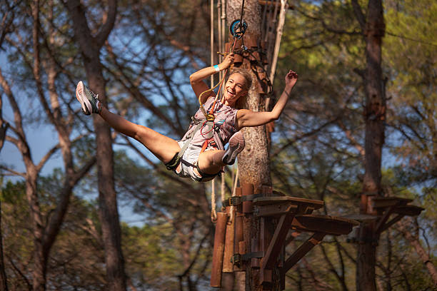 Young woman ziplining across an adventure rope course in a forest, feeling happy.