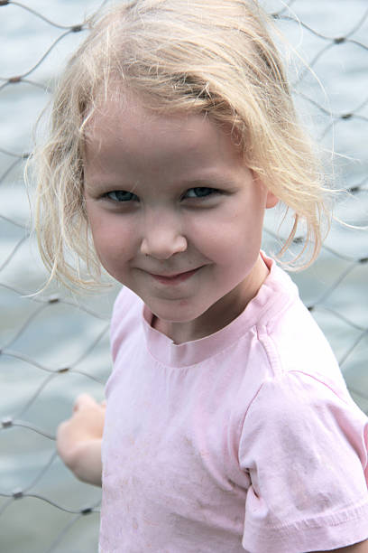 Portrait of a young girl smiling into the camera while holding on to a mesh wire fence.