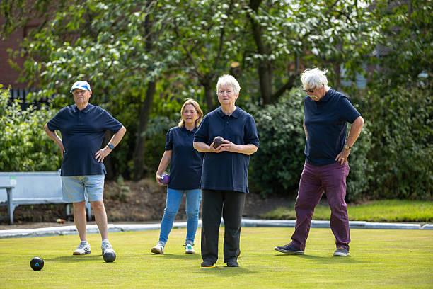 A wide shot of a group of four active seniors playing on a lawn bowling field in Leeds, West Yorkshire.