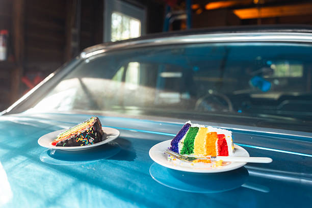 istock Two Rainbow Cake Slices Resting on a Classic Blue Car in Bright Sunlight 2238658729
