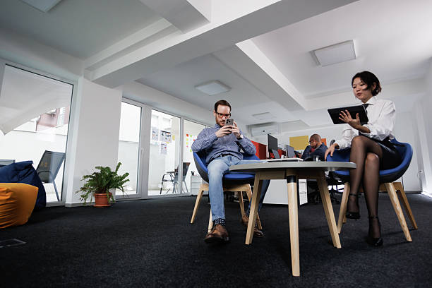 A diverse group of young professionals, including businesswomen and an African-American entrepreneur in a wheelchair, engage in collaborative discussion on various business projects in a modern startup office setting