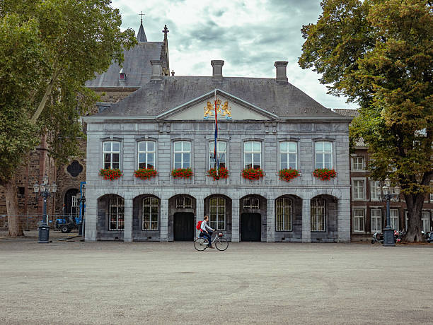 Maastricht, Netherlands – SEPTEMBER 9, 2018: The historic Hoofdwacht (Main Guard House) in Maastricht, featuring its gray stone facade and arched ground floor, with a person cycling past.