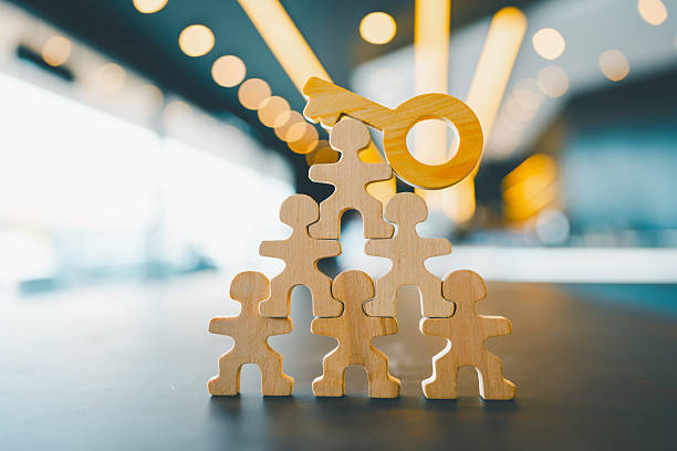 Wooden human figures forming a pyramid with a key symbol, representing teamwork, leadership, success, and human resources. Ideal for business concepts, strategy, or collaboration themes.