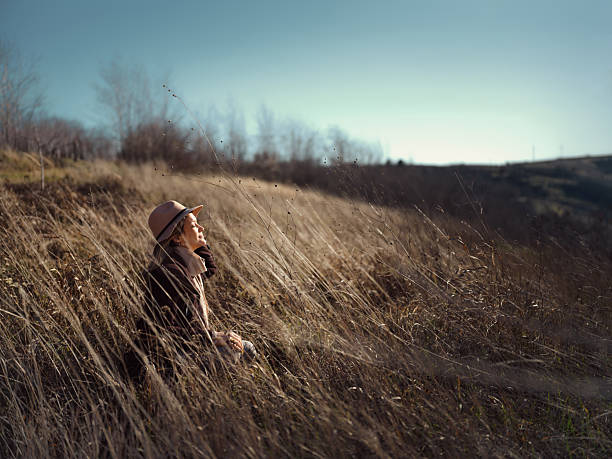 Young smiling woman relaxing in tall grass with her eyes closed during autumn day on a hill. Photographed in medium format. Copy space.