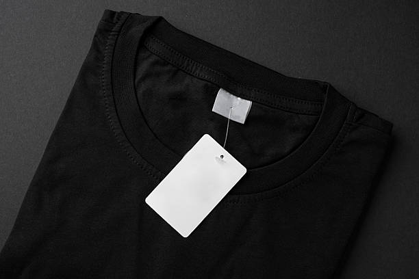 istock Folded black t-shirt with blank paper tag on dark background 2238687004