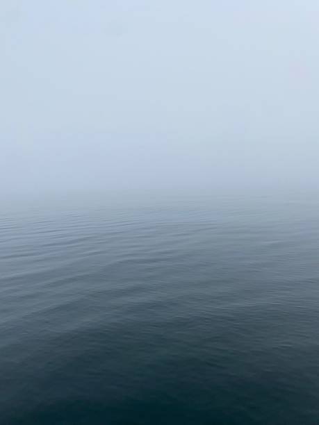A flat sea with grey/blue fog in the background