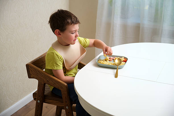 istock Sad boy eating pasta with sausages and cherry tomatoes on a white table from a portion plate. Childhood nutrition and daily meal concept. A child aged 4 years (four years old) 2238697543
