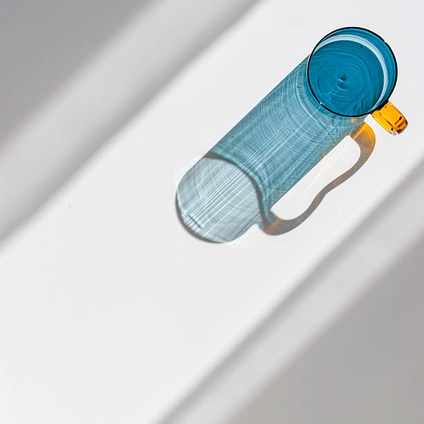 istock Blue colored glass mug with beautiful sunlight shadows on white. Top view yellow glass cup with Refraction at shiny drink, caustic effect, minimal aesthetic trend summer life style, copyspace 2238702405