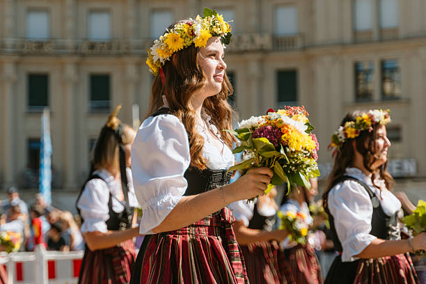 Munich, Germany - September 21, 2025:   Women wearing traditional dirndls walk in a festive parade, holding bouquets and wearing flower crowns, showcasing Bavarian culture and vibrant community spirit.