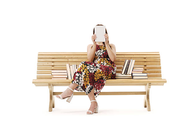 Woman sitting on a bench and showing a book with a blank cover, she is hiding her face: reading and literature concept