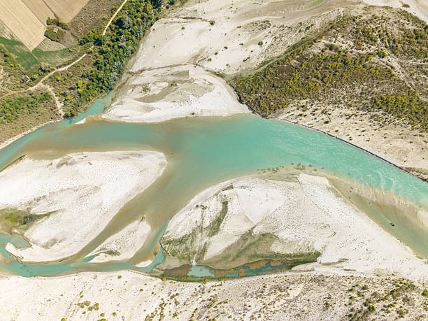 Overhead shot of a river splitting into multiple branches surrounded by sandy banks and green vegetation. Aerial landscape showing water flow and natural terrain patterns. River and nature scene from above.