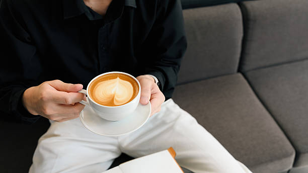 Peaceful break time with a close-up image of a man in black shirt holds latte with latte art in cafe