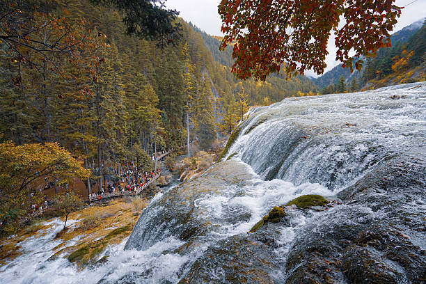 Waterfall flowing over rocks with autumn forest and tourists walking on trail