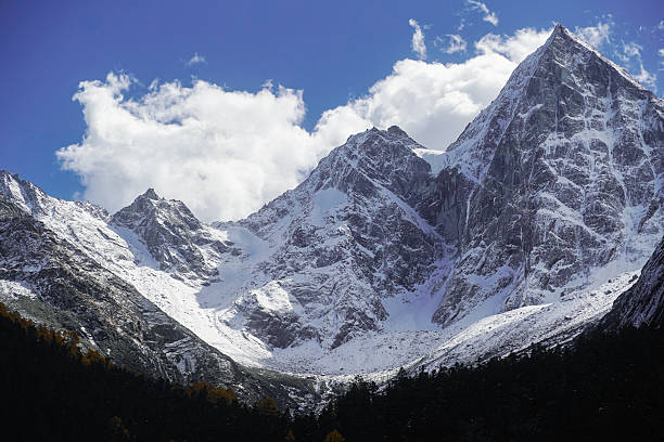 istock Snowy mountain peak with forest below under blue sky and white clouds 2238731050