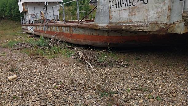 A Decaying Boat  Lies Stranded on a Pebbled Shore — Rusty, Forgotten, and Embraced by Nature’s Quiet Reclamation
