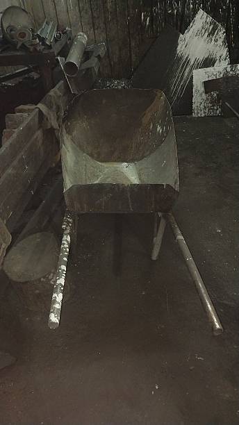 istock Rusty, empty wheelbarrow sits in a dark, cluttered workshop — worn, industrial, and full of untold stories. 2238739310