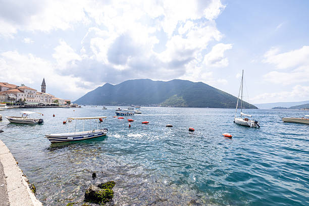 Several small boats moored near a stone pier in a calm coastal harbor with a mountainous island in the background. Scenic seaside village with clear blue water and cloudy sky. Maritime landscape with boats and waterfront buildings.