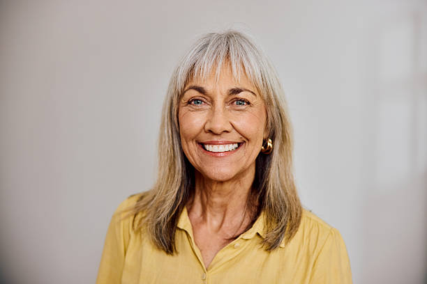 istock Confident older woman with hair bangs smiling at camera while standing against softly lit grey background 2238751117