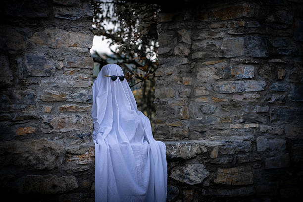 istock A figure in a flowing white sheet sits on a stone wall wearing black sunglasses 2238756038