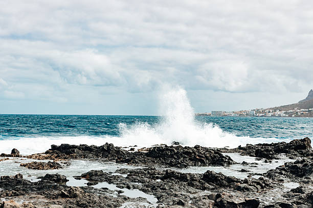 A beautiful side view of a huge wave splashing against coastal rocks in the Atlantic Ocean on an island on a cloudy autumn day. Concept: beautiful nature backgrounds and wallpapers.