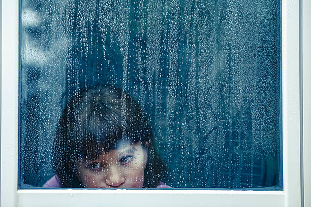 istock Girl peeking through rain-streaked window looking sad 2238757403