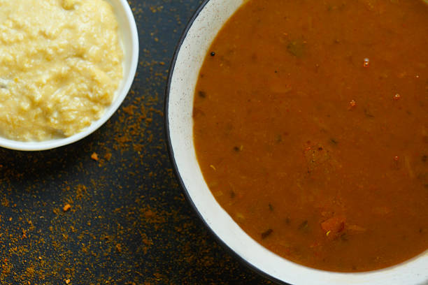 A delicious bowl of hot South Indian sambar served with coconut chutney on a rustic dark background, garnished with spices