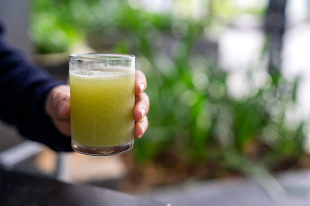 Close-up of a hand holding a glass of freshly blended celery juice, highlighting healthy eating, organic drinks, and wellness trends at home.