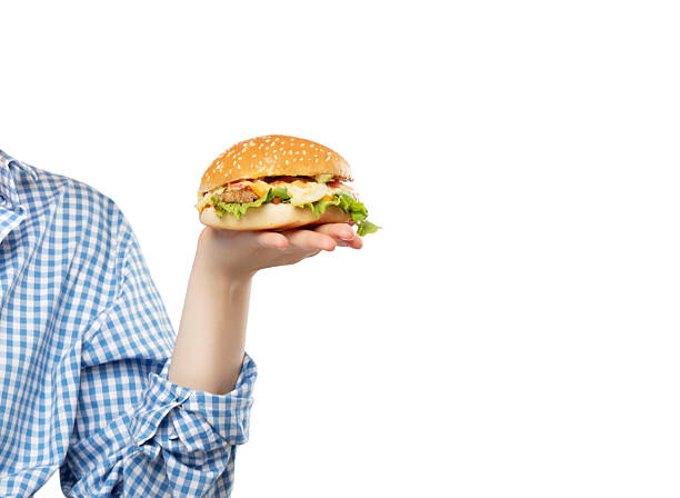 A young blonde girl with beautiful makeup in a blue shirt eats a hamburger on a white background.
