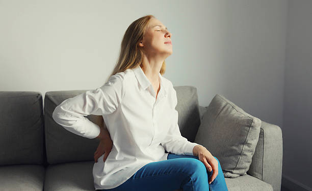 istock Woman suffering from back pain while sitting on couch at home 2238790174