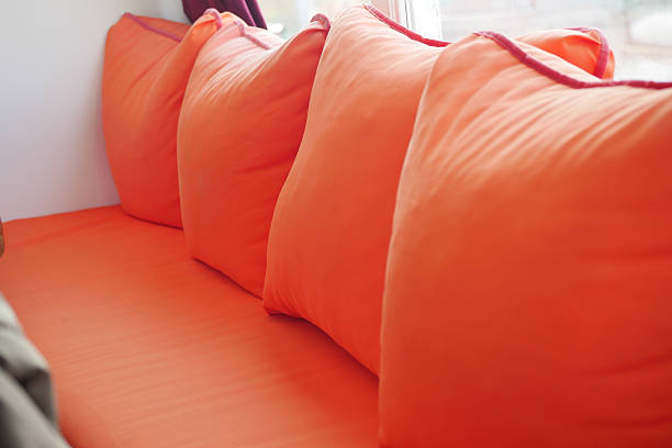 Cushions in vibrant orange colors line a comfortable couch in natural light.