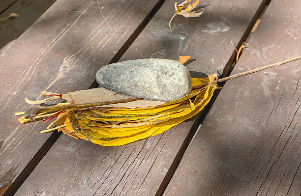 A collection of vibrant yellow autumn leaves and a smooth stone rest on a weathered wooden surface, bathed in sunlight.