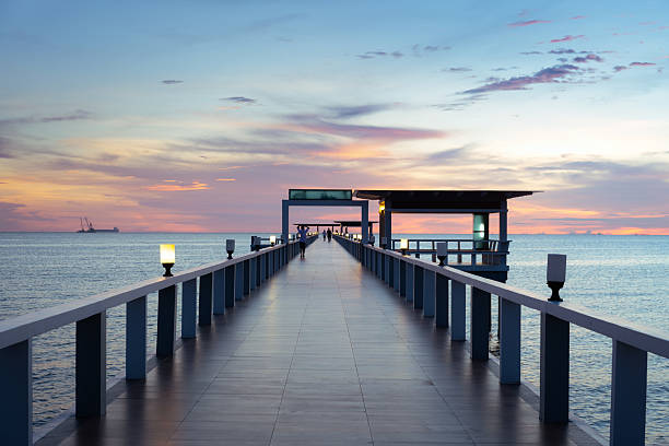 istock Long pier floor stretches toward horizon with pavilion under dark twilight sky, silhouetted against vibrant gradient of dusk. Scenic seascape background representing tranquility and relaxation. 2238799996