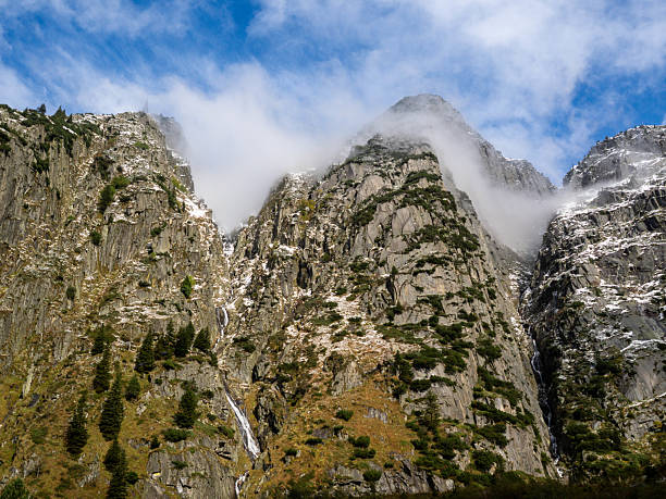 Majestic rocky mountain pass covered with patches of snow and mist under a blue sky. A breathtaking alpine landscape symbolizing adventure, wilderness, and natural beauty.